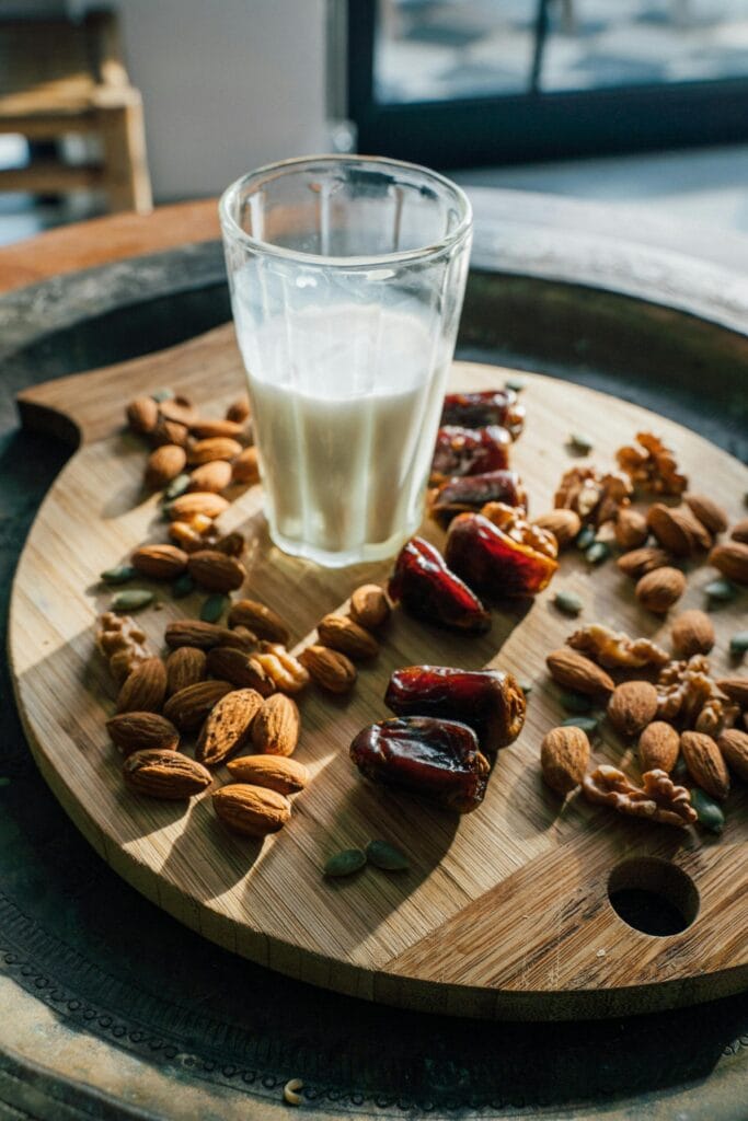 A wooden board with almonds, dates, and a glass of milk, beautifully lit for a Ramadan-themed still life.